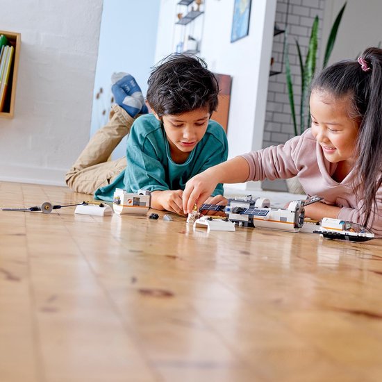 Twee kinderen leggen LEGO Ruimtevaart onderdelen uit. Een jongen met een groene trui en een meisje met een roze trui.