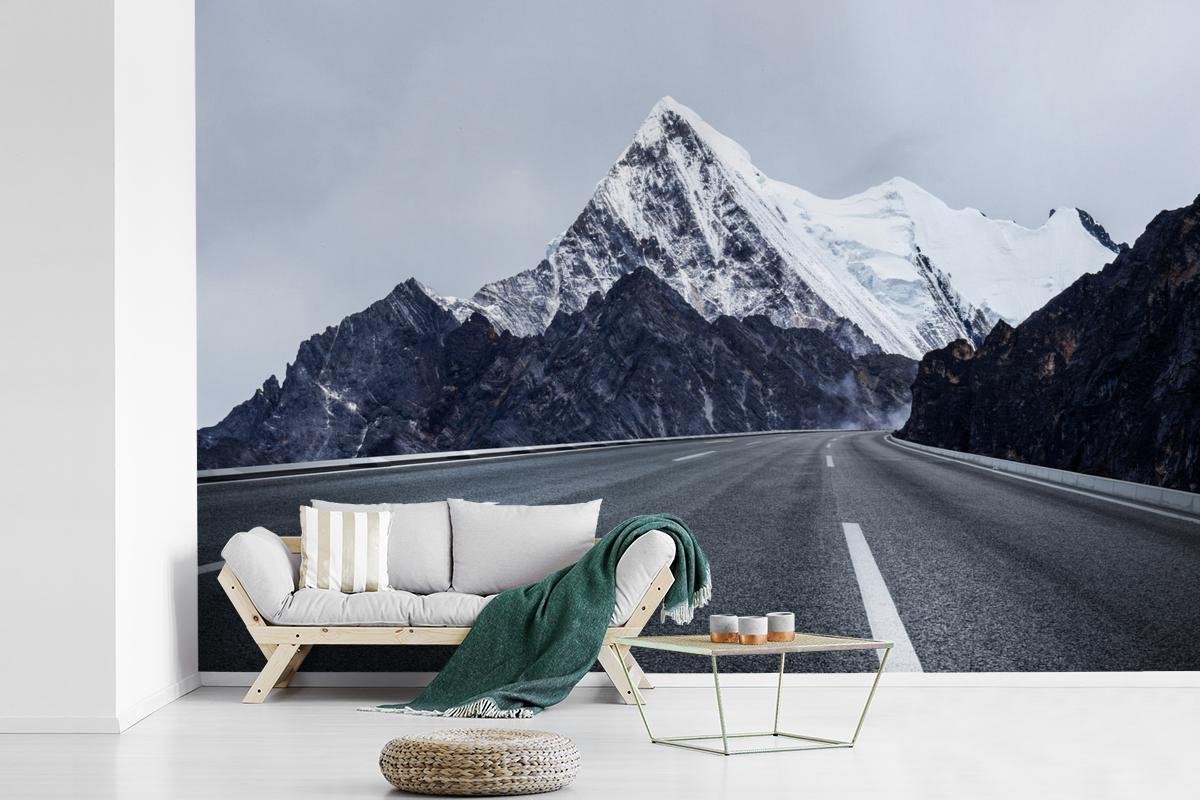 Behang - Fotobehang Zwart-wit foto van een weg door besneeuwde bergtoppen - Breedte 600 cm x hoogte 400 cm