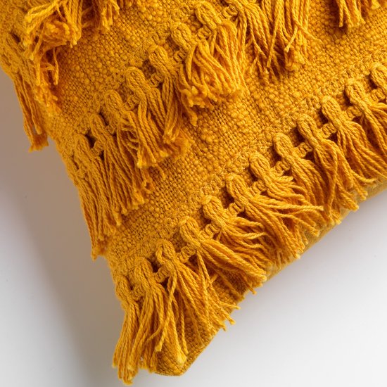 Détail du coussin décoratif ocre avec motifs brodés et franges.