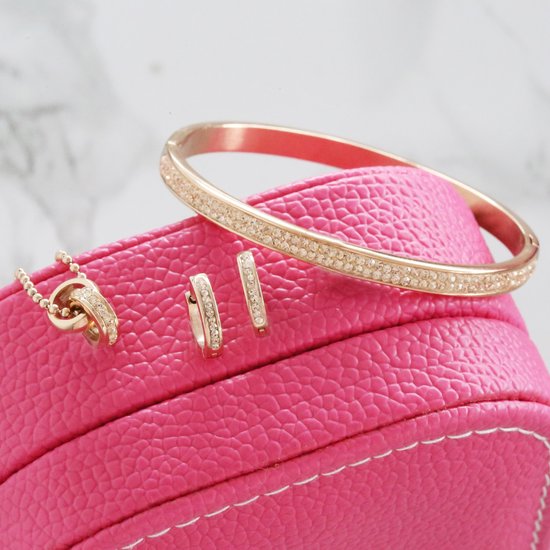 Gouden ketting, oorbellen en armband met kristallen op een roze doos.