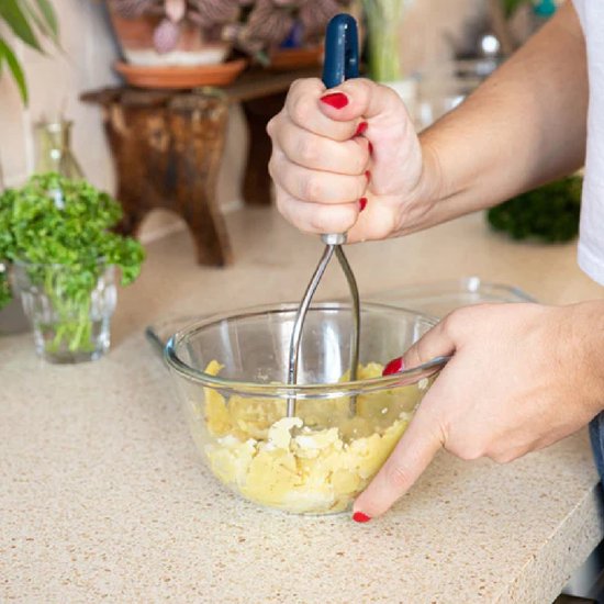 Handen met een aardappelstamper stampen aardappelen in een glazen kom.