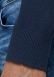 Arm en boord van een donkerblauwe coltrui, gedragen met een spijkerbroek.