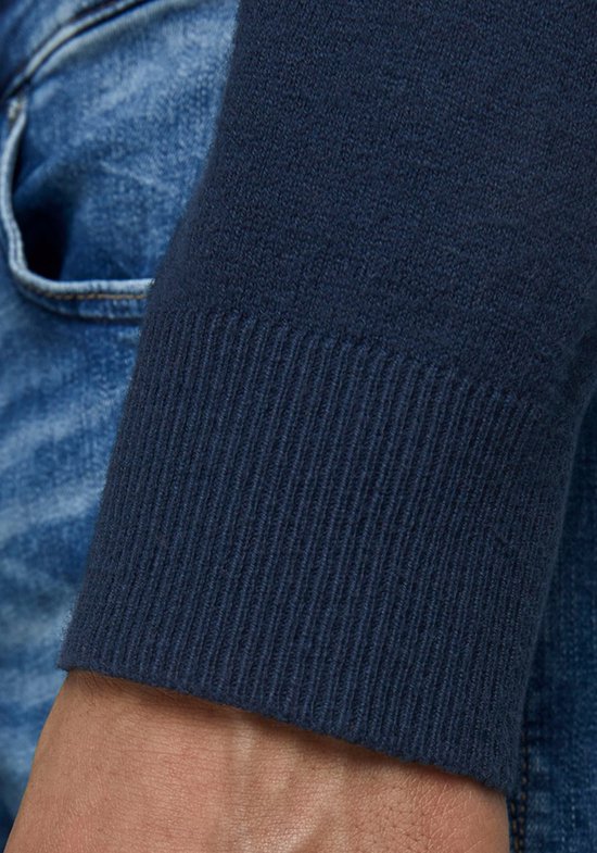 Arm en boord van een donkerblauwe coltrui, gedragen met een spijkerbroek.