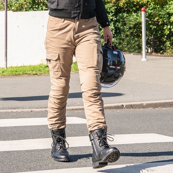 Vrouw kruist een zebrapad, draagt zandkleurige cargobroek en zwarte laarzen, houdt een helm vast.