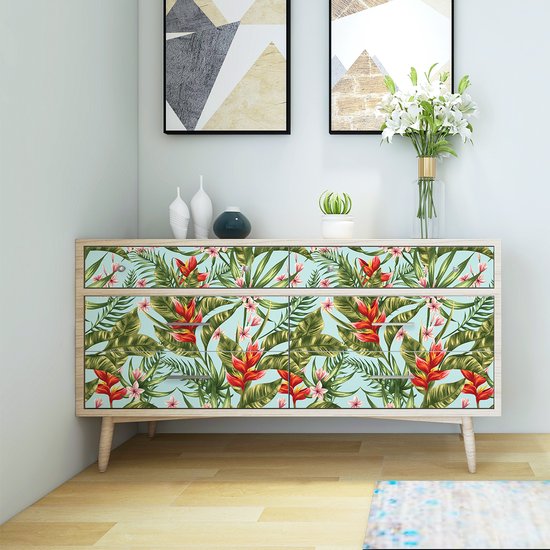 Sticker meuble bleu clair avec imprimé tropical de fleurs rouges, feuilles vertes et fleurs roses sur une commode claire.