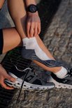 Een persoon trekt een grijze en witte sportsok aan bij een grijze hardloopschoen.