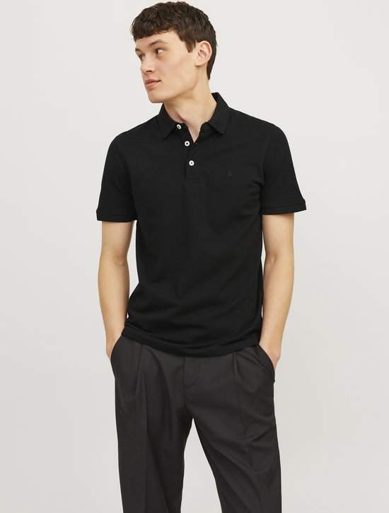 Man in een zwart poloshirt met korte mouwen, met de handen in de zakken.