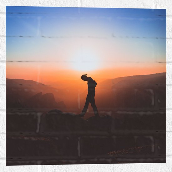 WallClassics - Muursticker - Silhouet Persoon tussen de Bergen bij Zonsondergang - 50x50 cm Foto op Muursticker