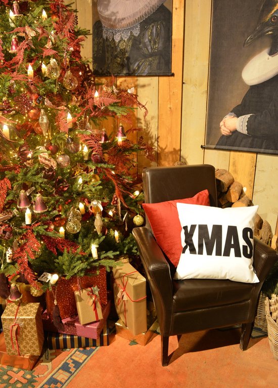 Bruin leren fauteuil met twee kerstkussens, één wit met zwarte tekst 'XMAS' en één rood.