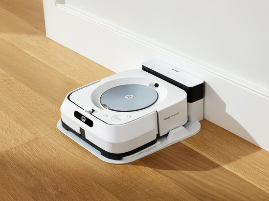 Witte robotdweilrobot met laadstation in de hoek van een kamer.