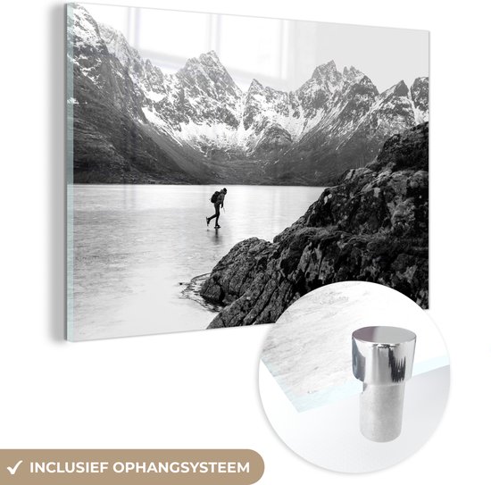 MuchoWow® Glasschilderij 150x100 cm - Schilderij acrylglas - Schaatser in een winters landschap met bergen - zwart wit - Foto op glas - Schilderijen