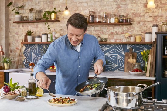 Jamie Oliver voegt ingrediënten toe aan een bord vanuit een zwarte koekenpan.