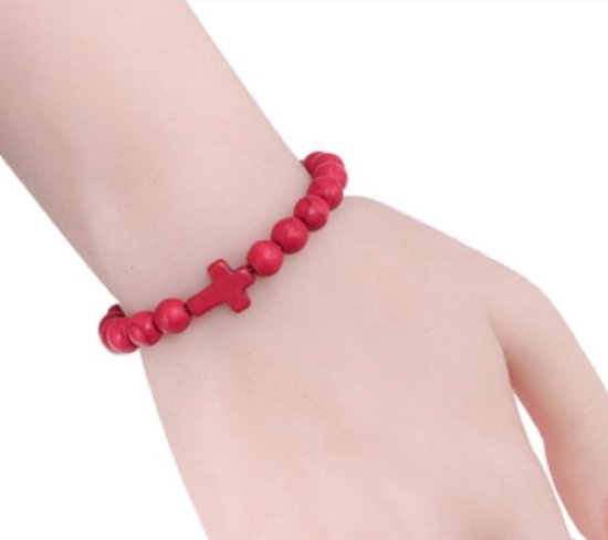 Een rode kralenarmband met rode kruisbedel, gedragen op een pols.