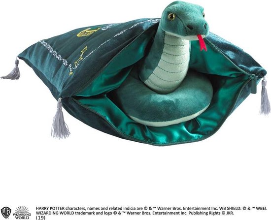 Serpent en peluche vert avec la langue sortie, posé sur une housse de coussin vert foncé ornée d'étoiles dorées et de glands.