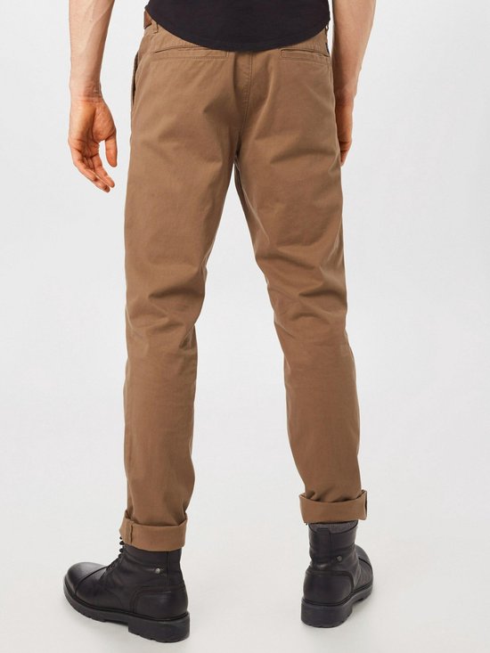 Achterkant van een lichtbruine chino broek voor heren, met omgeslagen broekspijpen en zwarte laarzen.