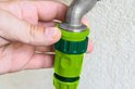 Hand koppelt groene slangstukken aan een kraan.