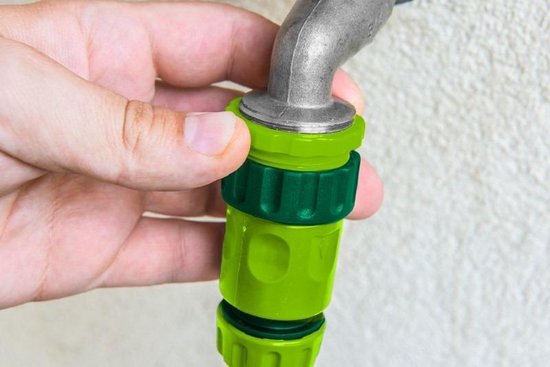 Hand koppelt groene slangstukken aan een kraan.