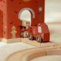 Houten brandweerwagen met ladder, op een houten treinbaan bij een rode brandweerkazerne.