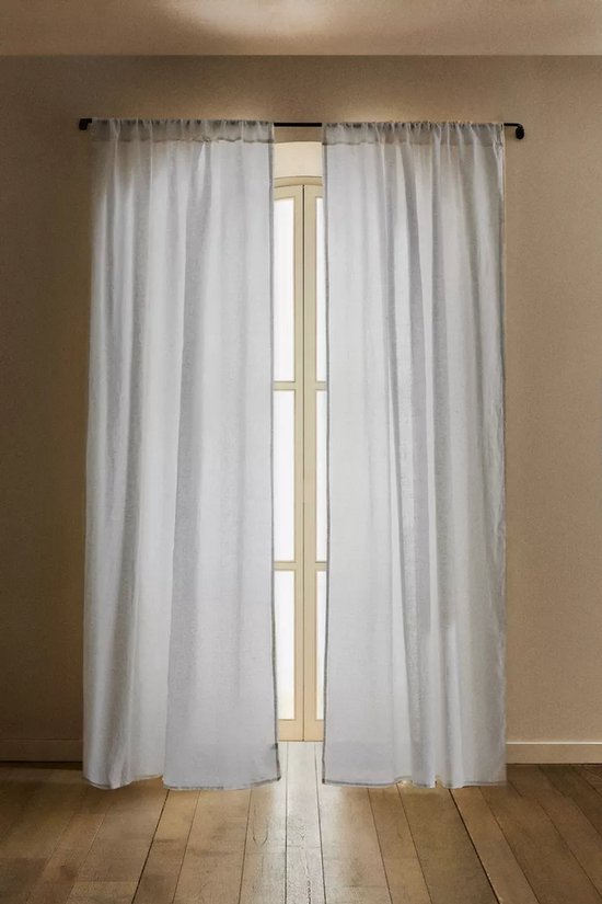 Twee witte linnen gordijnen hangen voor een deuropening met glas. De gordijnen hebben ruches aan de bovenkant en beige biezen.