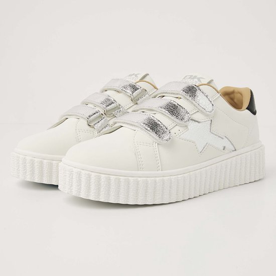 Paar witte leren sneakers met zilveren ster en bliksemschichtdetail, drie klittenbandsluitingen en dikke crèmekleurige zool.