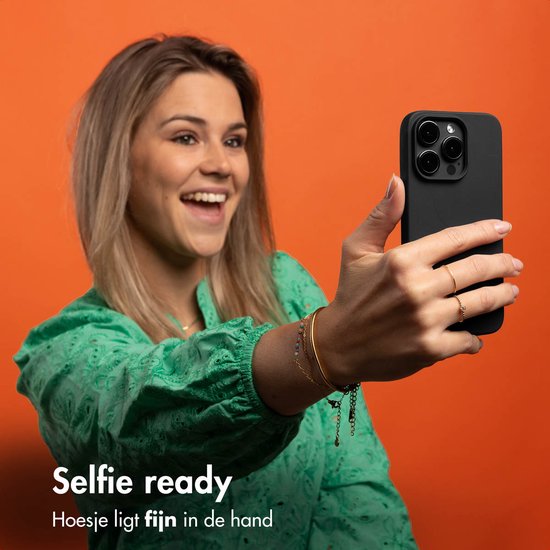 Une femme en haut vert prend un selfie avec sa coque de téléphone noire.