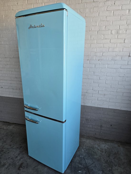 Hemelsblauwe Helvetia koel-vriescombinatie met zilveren handgrepen, staand tegen een witte bakstenen muur.