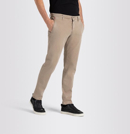 Man in beige chino broek met zwarte sneakers en zwarte T-shirt, handen in zakken.