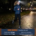Een rennende vrouw in de regen met een King Mungo hoofdlamp op haar hoofd, in een parkachtige omgeving.