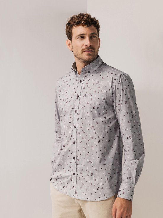 Man met een grijs overhemd met een all-over bloemenprint en beige broek.