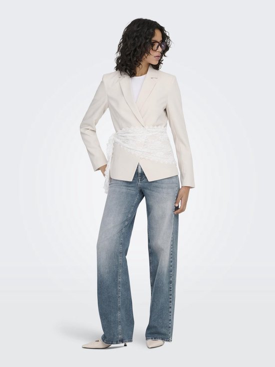 Model in een crème blazer met kanten ceintuur en wijde blauwe jeans.