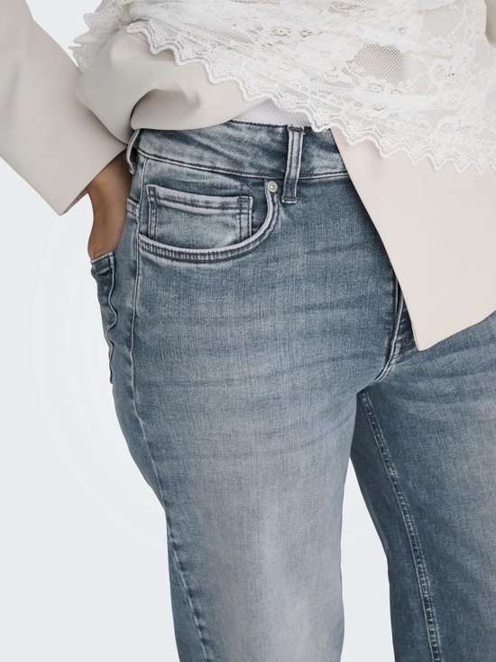 Dichtbij van de tailleband en zak van een lichtblauwe spijkerbroek. Model draagt een witte top met kanten details.