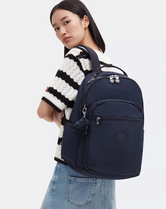 Femme portant un sac à dos Kipling bleu foncé avec un porte-clés singe bleu foncé, sur un haut rayé.