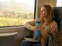 Vrouw met blauwe drinkfles kijkt uit het raam van een trein.