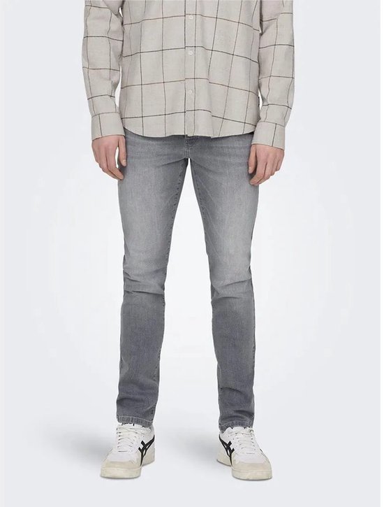 Man in grijze jeans en een beige geruit overhemd, gezien vanaf de voorkant.
