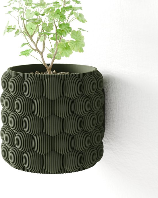 Een groene hangende plantenbak met een bubbelpatroon, met een plant erin, op een witte muur.