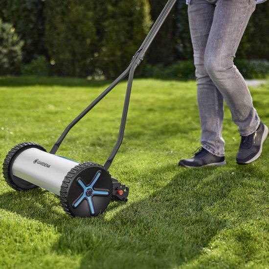 Persoon maait gras met GARDENA kooimesmaaier. Grijze jeans, zwarte schoenen.