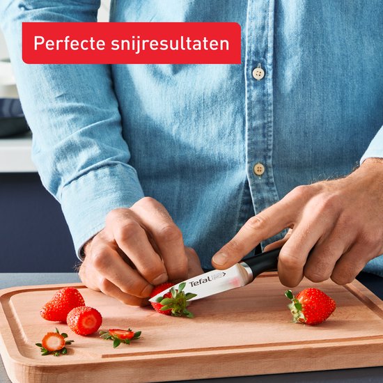 Hand snijdt aardbeien met Tefal mes op snijplank