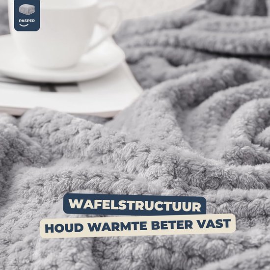 Detailopname van de grijze wafelstructuur van de deken, met een kopje koffie.