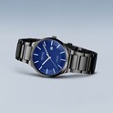 Zwart titanium herenhorloge met blauwe wijzerplaat, datumvenster en zilverkleurige indexen, zwevend.