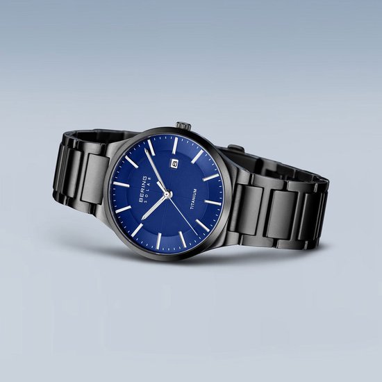 Zwart titanium herenhorloge met blauwe wijzerplaat, datumvenster en zilverkleurige indexen, zwevend.