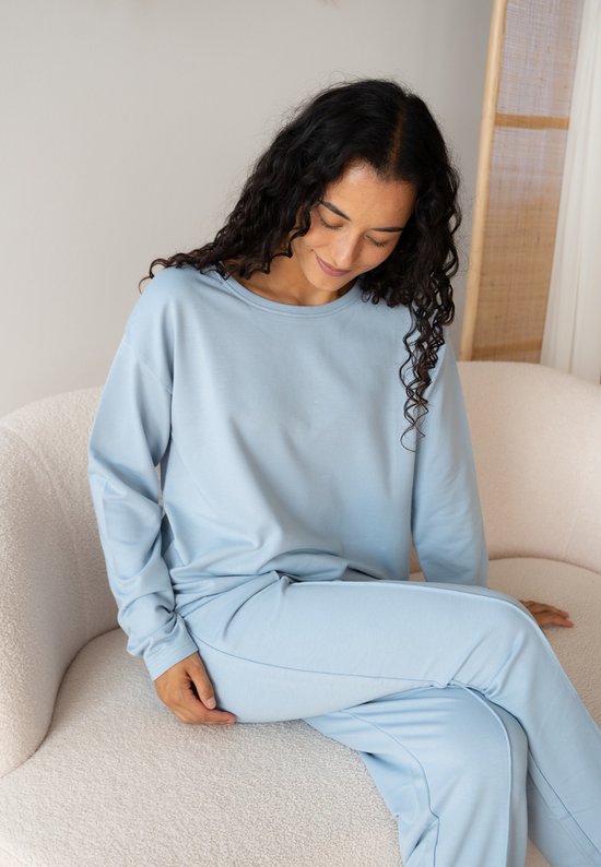 Model in een lichtblauwe loungewear set bestaande uit een trui met lange mouwen en een joggingbroek.