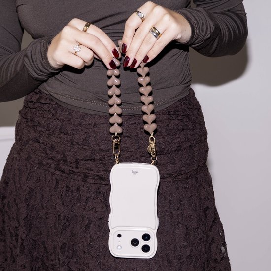 Off-white golvend telefoonhoesje met bruine hartjeskoord, gedragen door een persoon in bruine kleding.
