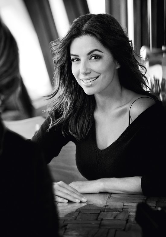 Model met lang, donker haar, draagt een off-shoulder trui en glimlacht.