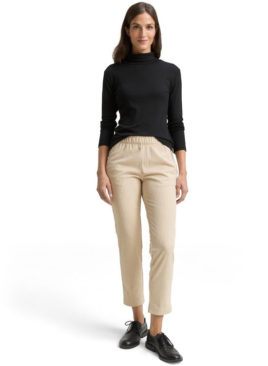 Vrouw draagt een zwarte coltrui en een beige corduroy broek.