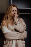 Vrouw met lang blond haar in een satijnen badjas en kanten bh.