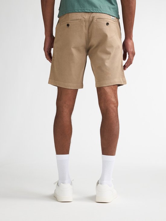 Man van achteren gezien in een beige chino short met een groene t-shirt, witte sokken en sneakers.