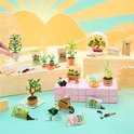 Miniatuur tuin scène met verschillende plantjes in potjes, een kruiwagen, gieter en zakjes potgrond.
