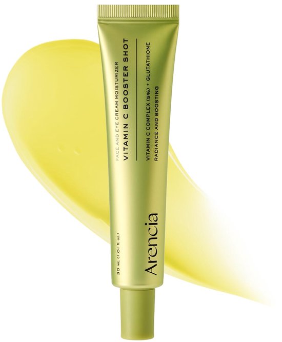 Gouden tube met groene dop, met 'Vitamin C Booster Shot' erop. Een heldergele veeg crème textuur is op de achtergrond.