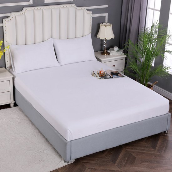 Drap-housse blanc sur un lit fait avec des oreillers blancs et une tête de lit grise.