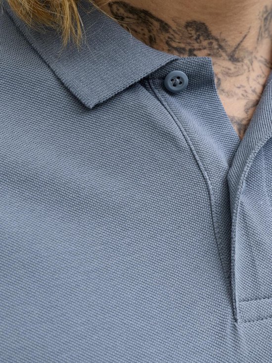 Sluiting van een blauw poloshirt met knoop en geborduurd '&'-symbool op de borst.